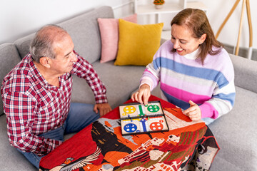 Happy senior couple playing board game at home