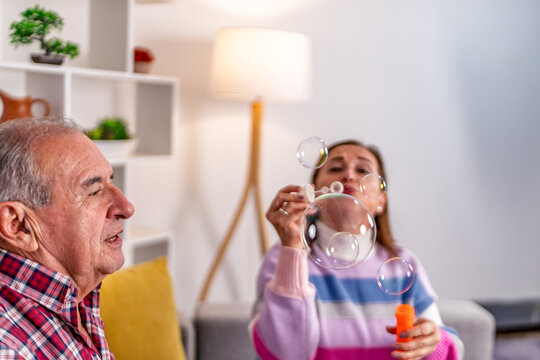 Daughter blowing soap bubbles while having fun with elderly father at home