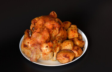 Whole baked chicken with new potatoes on a white ceramic plate on a black background.