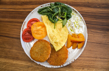 Delicious and colorful breakfast featuring omelette, fresh vegetables, ripe fruit, and crispy potato pancakes displayed on vibrant plate, served on rustic wooden table, for perfect morning start