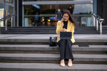 Fototapeta premium Businesswoman working remotely on stairs while talking on phone