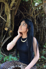 Modelo latina posando frente a un fondo de ramas, usando un conjunto de moda y accesorios. Concepto de moda, belleza y estilo.