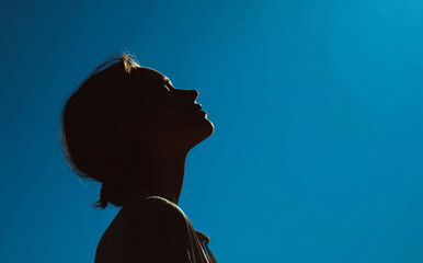 Silhouette of young woman gazing at clear blue sky, evoking sense of tranquility and contemplation