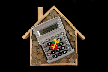 A symbolic wooden house filled with 100 and 200 Kazakhstani tenge coins, gift box and calculator 