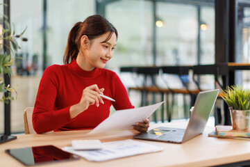 Smiling Asian Business woman using calculator and laptop for doing math finance on an office desk, tax, report, accounting, statistics, and analytical research concept
