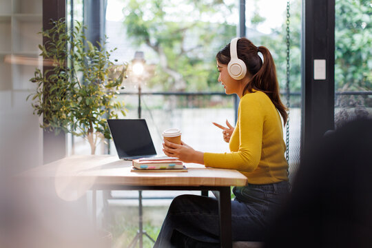 Happy asian girl college student wearing headphones watching distance online class, remote university webinar or having talk on laptop video conference call virtual meeting at home or campus.
