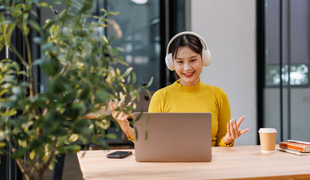 Happy asian girl college student wearing headphones watching distance online class, remote university webinar or having talk on laptop video conference call virtual meeting at home or campus.
