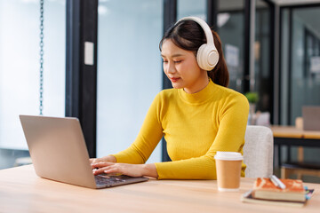 Portrait of Young Asian woman sitting at desk and connecting with her laptop, she is wearing...
