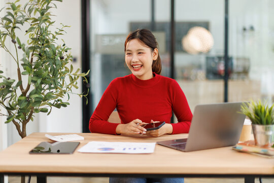 Smiling and happy millennial Asian business young woman chatting with her friends on her phone while relaxing in the office.
