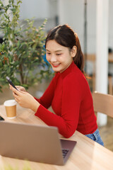 Shot of a asian young business Female working on laptop computer and holding phone in her...