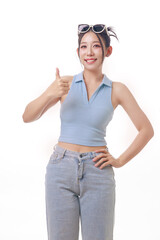 Cheerful young woman giving a thumbs up in a stylish sleeveless top and denim jeans over a white...