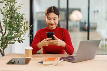 Shot of a asian young business Female working on laptop computer and holding phone in her...