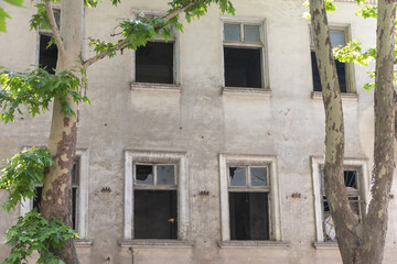 The facade of an old building with broken windows, trees in front, view from the street
