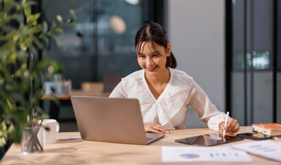 Young Asian professional business woman office worker analyst sitting at desk working on laptop...