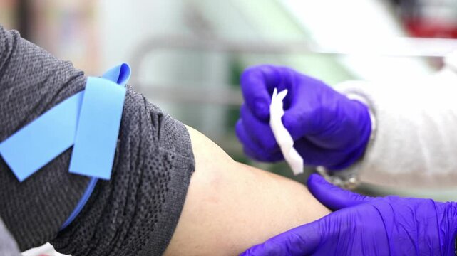 Healthcare worker wearing gloves prepares a patient's arm with a tourniquet for blood extraction