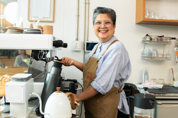 A confident senior coffee shop owner stands behind cafe bakery counter with arms crossed....