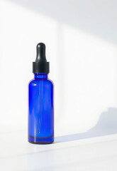Blue glass dropper bottle with black cap, placed on white surface under soft natural light. Minimalist and clean design