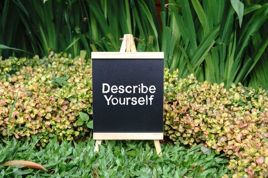 Describe Yourself writing concept on a small blackboard with a background of trees.