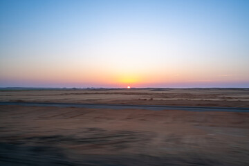 A breathtaking sunrise painting the vast Aswan desert in Egypt, seen from a moving vehicle on the...