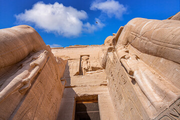 A dramatic low-angle view of the entrance to the Great Temple of Ramses II at Abu Simbel, Aswan, Egypt, showcasing the colossal statues and intricate carvings under a bright sky.