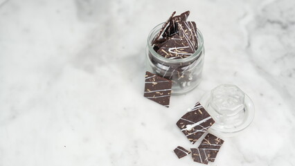 Crispy brownies arranged on a glass jar and white ceramic plate with a white marble background....