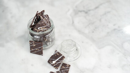 Crispy brownies arranged on a glass jar and white ceramic plate with a white marble background....
