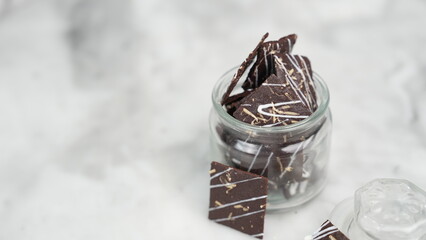 Crispy brownies arranged on a glass jar and white ceramic plate with a white marble background....