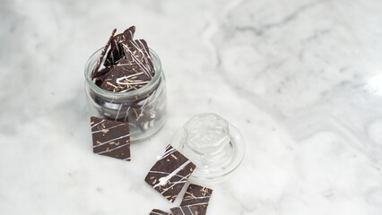 Crispy brownies arranged on a glass jar and white ceramic plate with a white marble background....