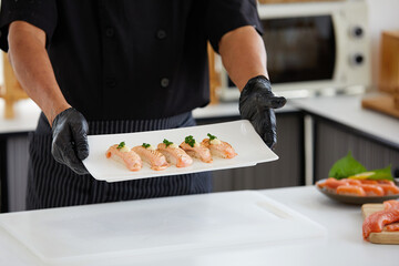 close up chef holding and showing salmon sushi on white plate