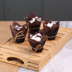 catherine chocolate cake wrapped in brown cake paper and tied with hemp rope, arranged on a hollow wooden baking tray