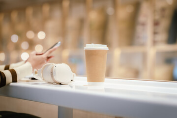 Young Asian woman sitting in a cozy café, smiling while using her smartphone and laptop, enjoying a hot drink, studying, working, and relaxing in a modern setting.