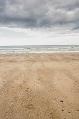 Flat design is showing beach with pebbles and shells meeting calm sea under dark clouds