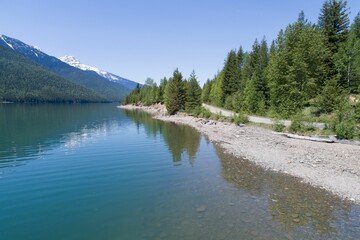 Trees growing at shore by mountain range against clear sky