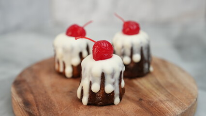 Three pieces of Chanelle cheesecake with white chocolate topping and red cherries placed on a round wooden plate