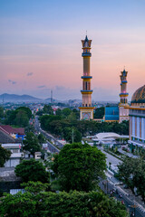 Obraz premium Golden twilight blankets the majestic mosque in Mataram city, Lombok, highlighting elegant minarets, vibrant streets, and surrounding hills under a serene pastel sky. Masjid Islamic Center Mataram.