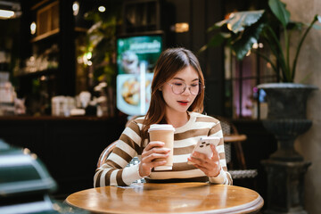 A stylish young woman with glasses and braces smiles at the camera, holding a coffee cup in a warmly lit cafe setting.