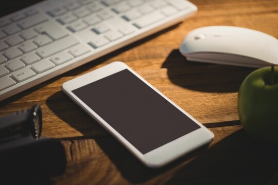 Fototapeta Smartphone is sitting on wood desk in flat design, with keyboard and mouse, flashlight, green apple