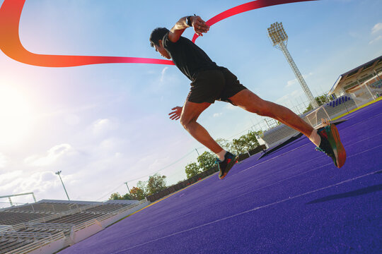 Fit young man running sprinting to red finish line at the racetrack. Finisher, marathon runner sprinting moment at the racetrack.
