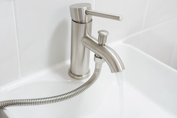 Water flows from a tap into a sink on a gray background close-up.