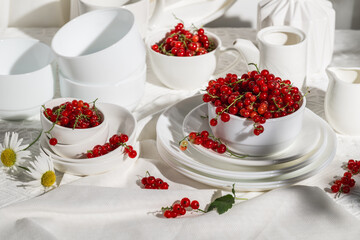 Bowls with red currants on table with white dishes. Summer still life.