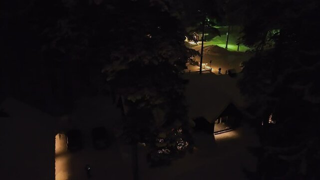 Aerial view of illuminated cabins in middle of trees, winter night in Finland
