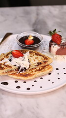 Chewy potato bread is arranged on a white plate and topped with cheese, strawberries and melted chocolate.