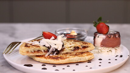 Chewy potato bread is arranged on a white plate and topped with cheese, strawberries and melted chocolate.