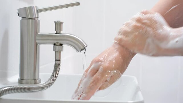 Woman washing hands with soapy foam over sink tap side view close-up.