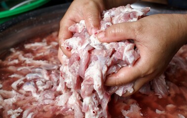 Both hands are holding small pieces of fatty pork in a stainless steel bowl. The concept of cooking, preparing ingredients and cleanliness is hygienic and healthy.