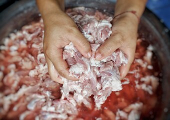 Both hands are holding small pieces of fatty pork in a stainless steel bowl. The concept of cooking, preparing ingredients and cleanliness is hygienic and healthy.