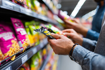 close-up of two hands comparing snack nutrition labels in supermarket aisle, 