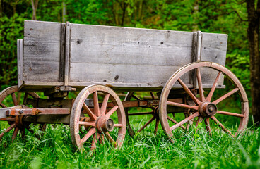 Vintage wooden cart with large wheels resting on a dusty floor in a rustic barn environment during...