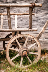 Vintage wooden cart with large wheels resting on a dusty floor in a rustic barn environment during...
