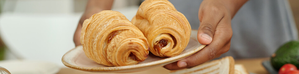 Close-up showing hands holding plate with freshly baked spiral pastries filled with sweet filling, revealing beautiful pastry layers and inviting texture
